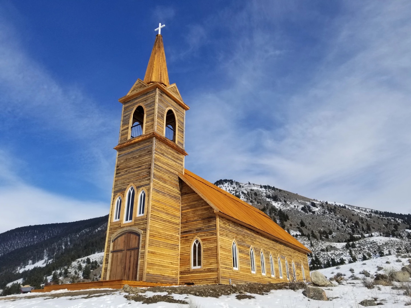 Wood-sided church with a bell tower and steeple on a snowy Montana hillside