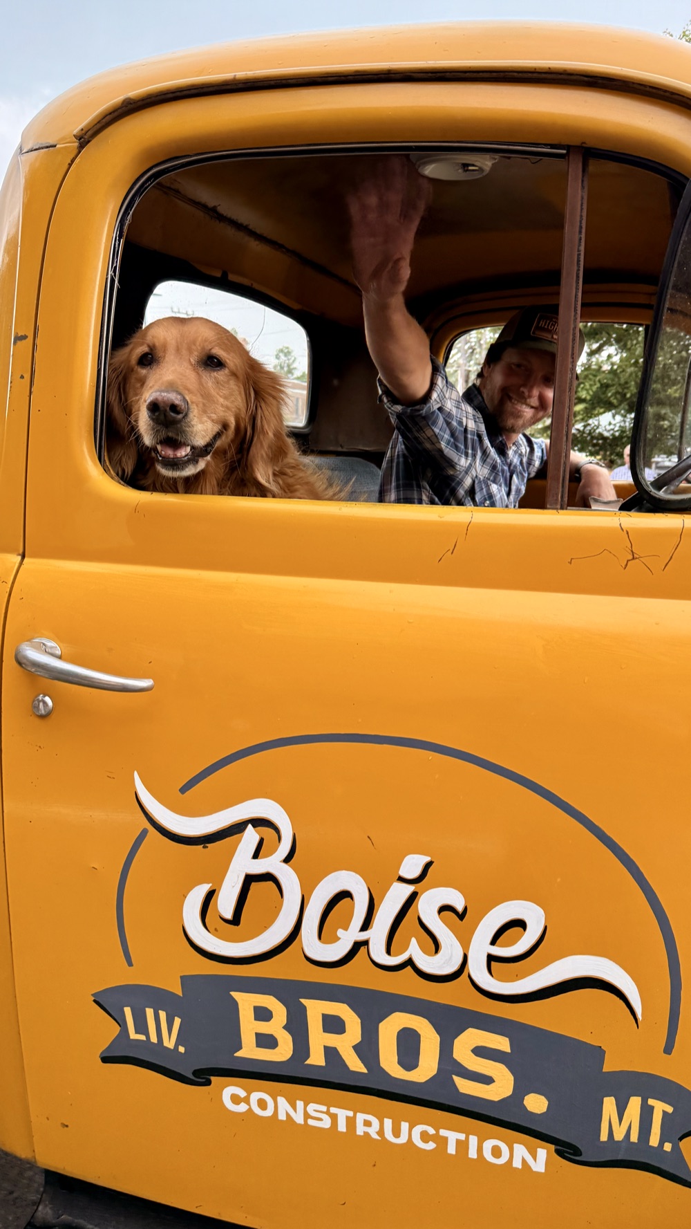 Michael Boise waving from the cab of the vintage Boise Bros. truck, with the shop dog riding shotgun